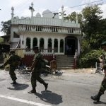 Security forces walk past a mosque that was damaged in the Kandy area