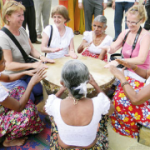 Tourists join village women in a round of traditional drumming.